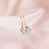 Delicate earrings with heart-shaped gemstones on a soft pink background